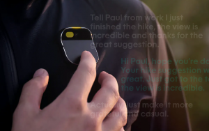 Un dispositivo AI pin colocado en la solapa de una persona. Aparecen mensajes de texto semitransparentes flotando en la imagen